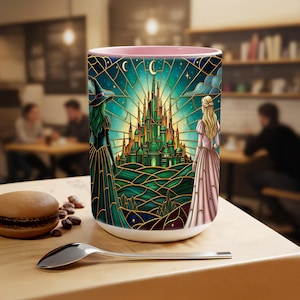 Puede incluir: Taza de cer&aacute;mica blanca con interior rosa, con un dise&ntilde;o de vidriera de un castillo verde, una bruja y una princesa. El dise&ntilde;o incluye una luna creciente y estrellas. La taza est&aacute; sobre una mesa de madera con una cuchara y un macaron.