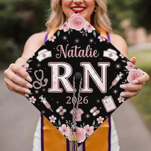 May include: A black graduation cap topper featuring the name Natalie, the letters R.N., and the year 2026. The design includes pink floral accents, medical icons like a stethoscope, syringes, pills, a clipboard, and nurse caps on a dark background.