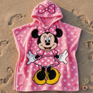 May include: Pink hooded beach towel featuring Minnie Mouse. The towel has a polka dot pattern and a large graphic of Minnie Mouse on the front. The hood has a bow on top.