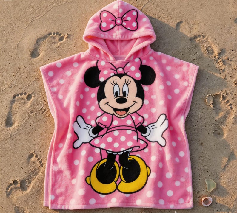 May include: Pink hooded beach towel featuring Minnie Mouse. The towel has a polka dot pattern and a large graphic of Minnie Mouse on the front. The hood has a bow on top.