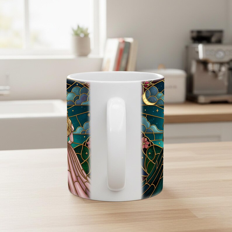 Puede incluir: Taza de cer&aacute;mica blanca con un dise&ntilde;o de vidriera. El dise&ntilde;o presenta a una mujer con un vestido rosa, una luna creciente y estrellas sobre un fondo verde azulado, todo delineado en dorado. La taza tiene un asa blanca.