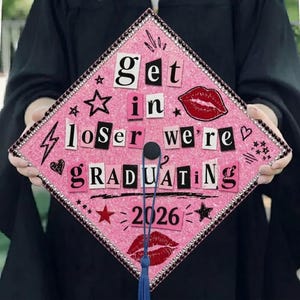 Puede incluir: Gorra de graduación rosa decorada con el texto "Get in loser we're graduating 2026". La gorra está adornada con pedrería, estrellas, corazones y un rayo. Una borla azul cuelga del centro.