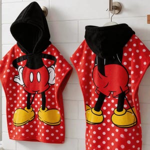 May include: Two red and white polka dot hooded bath towels featuring Mickey Mouse. The towels have a black hood and a large Mickey Mouse graphic on the front. The towels are hanging on a metal hook.