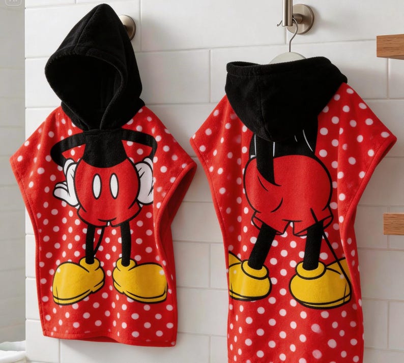 May include: Two red and white polka dot hooded bath towels featuring Mickey Mouse. The towels have a black hood and a large Mickey Mouse graphic on the front. The towels are hanging on a metal hook.