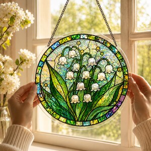 Pu&ograve; includere: Un acchiappasole circolare in vetro colorato che raffigura fiori di mughetto bianchi con foglie verdi. L'oggetto &egrave; incorniciato da un bordo di piccole tessere di vetro verdi e gialle ed &egrave; appeso a una sottile catena di metallo nero.