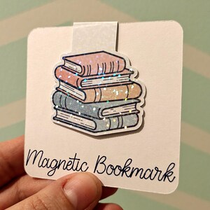Op de afbeelding: Een witte kaart met een stapel kleurrijke boeken met glitter. De kaart heeft onderaan de tekst "Magnetic Bookmark".