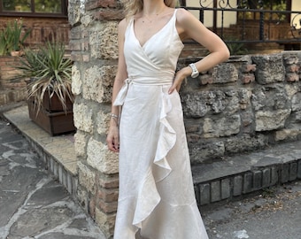May include: A cream-colored wrap dress with a V-neckline and a flowing, asymmetrical hem. The dress features a waist tie and ruffled detailing along the skirt. The person is wearing sunglasses and nude-colored heels.