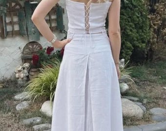 Puede incluir: Conjunto de dos piezas de lino blanco. El top corto tiene tirantes finos y espalda con cordones, combinado con una falda de cintura alta. La falda tiene una abertura en la espalda. El conjunto es de lino.