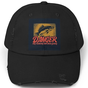 Op de afbeelding: Zwarte, verweerde baseballpet met een vintage-stijl afbeelding van een vis en de tekst "DANGER may randomly talk about fishing".