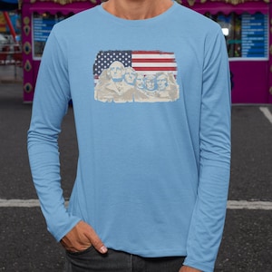 A person wearing a long-sleeved blue shirt with an American flag design featuring Mount Rushmore statues.