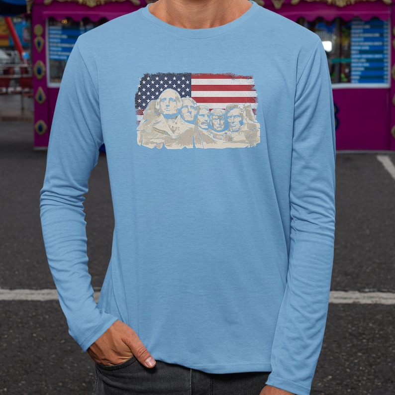 A person wearing a long-sleeved blue shirt with an American flag design featuring Mount Rushmore statues.
