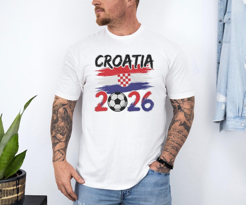 A man wearing a white t-shirt with the text "Cromia 2026" and a graphic of the Croatia national flag, standing in front of a plant and a denim jacket.