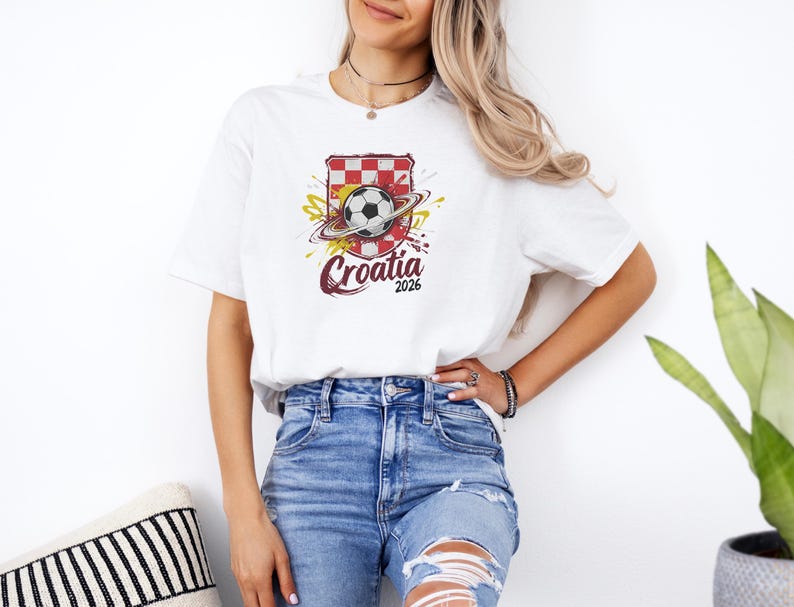A woman wearing a white t-shirt with a graphic of a soccer ball and the text "Croatia 2006" stands next to a potted plant.