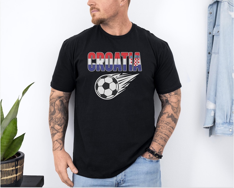 A man wearing a black t-shirt with the word "Croatia" printed on it, standing in front of a plant and a denim jacket.