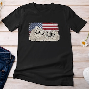 A black t-shirt with a graphic design featuring the Statue of Liberty and the faces of three other figures, all set against an American flag.