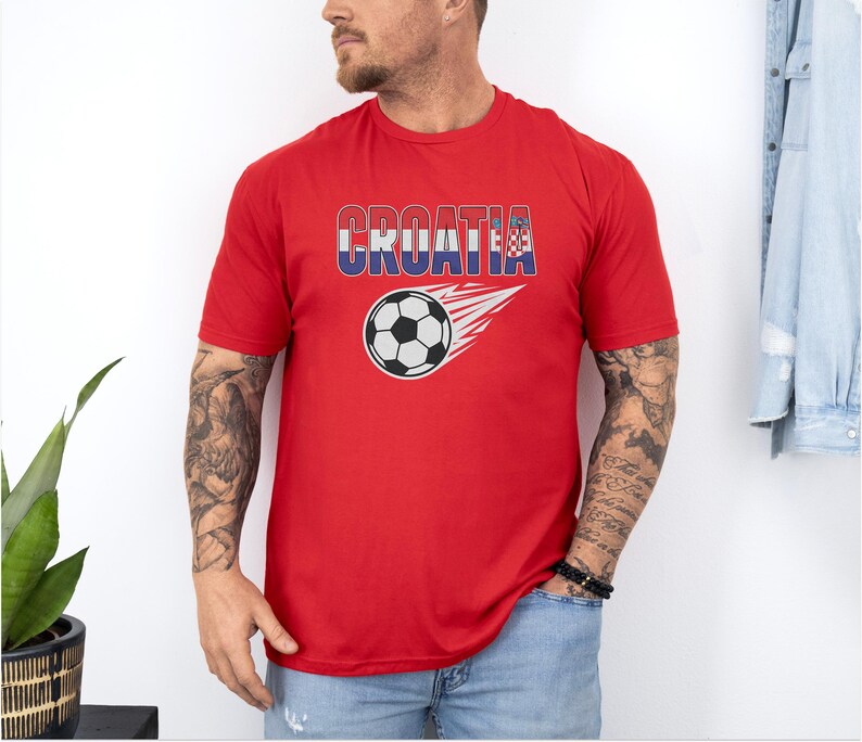 A man wearing a red t-shirt with the word "Croatia" printed on it, standing against a white wall.