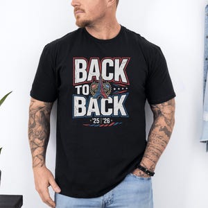 A man wearing a black t-shirt with the text "BACK TO BACK" printed on it, standing against a white wall.