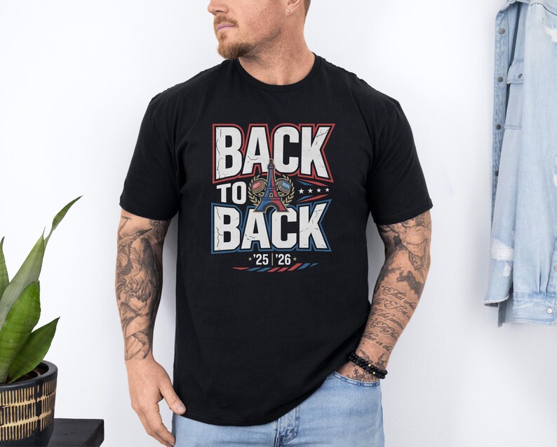 A man wearing a black t-shirt with the text "BACK TO BACK" printed on it, standing against a white wall.