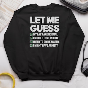 May include: Black sweatshirt with white text that reads "Let me guess" and a checklist with the following options: "My labs are normal", "I should lose weight", "I need to drink water", "I might have anxiety".
