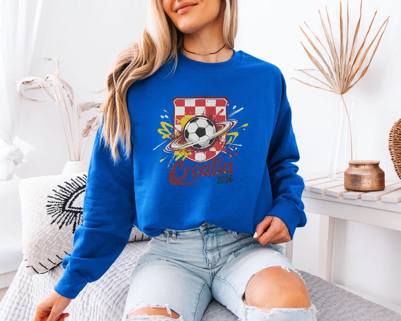 A woman wearing a blue sweatshirt with a soccer ball design and the text "Cristiano 2016" is sitting on a couch.