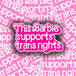 May include: A pink sticker with the text "This Barbie supports trans rights" in a stylized font. The sticker is outlined in white and set against a background of repeating text that reads "This Barbie supports trans rights".