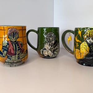 Puede incluir: Tres tazas de cer&aacute;mica con ilustraciones de personajes. La primera taza es naranja con un personaje con chaleco rojo. La segunda taza es verde con una ilustraci&oacute;n de personaje. La tercera taza es amarilla con un rayo en el asa.