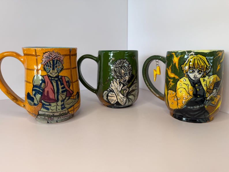 Puede incluir: Tres tazas de cer&aacute;mica con ilustraciones de personajes. La primera taza es naranja con un personaje con chaleco rojo. La segunda taza es verde con una ilustraci&oacute;n de personaje. La tercera taza es amarilla con un rayo en el asa.