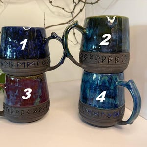 May include: Four ceramic mugs with handles, each featuring a dark, unglazed base band embossed with runic characters. Mug 1 is deep blue, mug 2 is dark green and blue, mug 3 is a mix of red and purple, and mug 4 is a vibrant blue and teal blend.