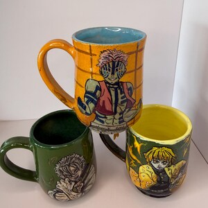 Puede incluir: Tres tazas de cer&aacute;mica con ilustraciones de personajes. Una taza es naranja con interior azul y dise&ntilde;o de personaje. Otra es verde con dise&ntilde;o de personaje. La tercera es amarilla con dise&ntilde;o de personaje.