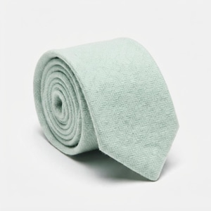 Puede incluir: Una corbata enrollada de color verde menta suave con un sutil patr&oacute;n de tejido en espiga. La tela tiene una apariencia texturizada con un acabado mate, y la corbata est&aacute; enrollada en forma circular, mostrando la pala frontal y las capas internas.