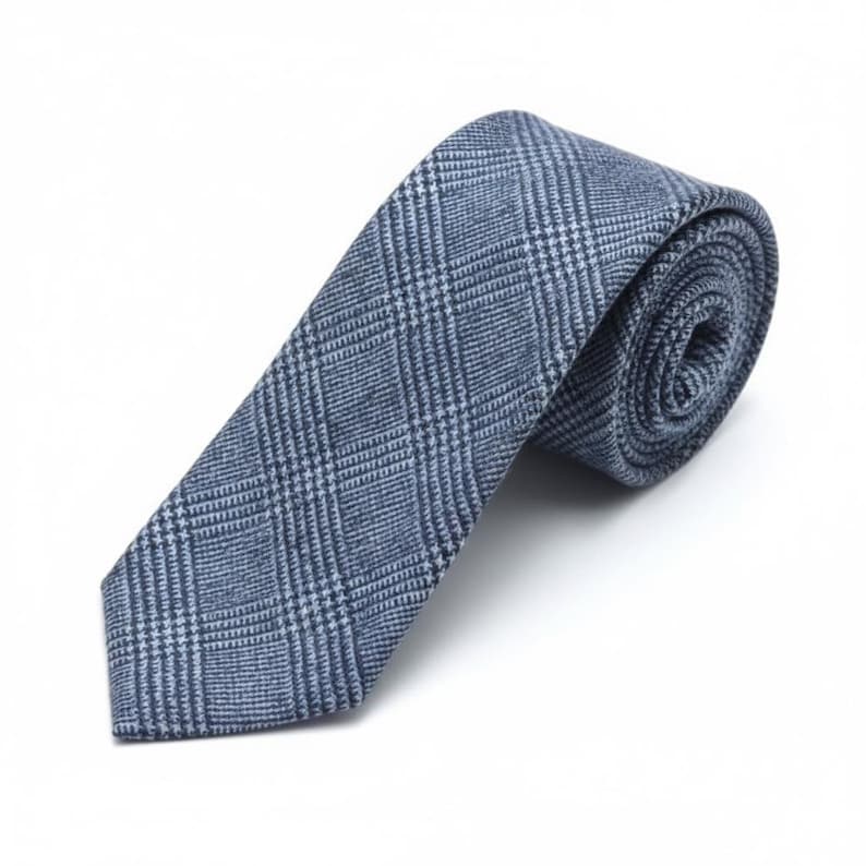 Puede incluir: Una corbata azul y blanca con un patr&oacute;n cl&aacute;sico de cuadros pr&iacute;ncipe de gales. La tela tiene una apariencia texturizada con un acabado tejido. La corbata est&aacute; enrollada en la parte superior y se estrecha hacia una punta, mostrando un dise&ntilde;o de cuadr&iacute;cula.