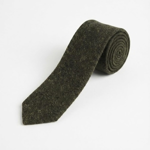 Puede incluir: Una corbata de color verde oliva oscuro con una apariencia texturizada y moteada. La corbata est&aacute; enrollada en el extremo superior, mostrando una estructura en espiral, mientras que la pala puntiaguda se extiende hacia abajo con un tejido uniforme.