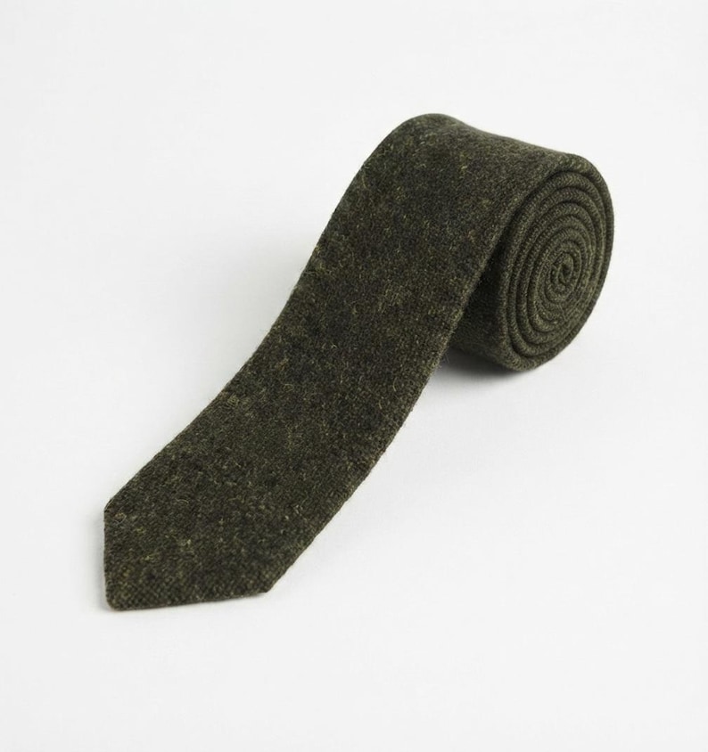 Puede incluir: Una corbata de color verde oliva oscuro con una apariencia texturizada y moteada. La corbata est&aacute; enrollada en el extremo superior, mostrando una estructura en espiral, mientras que la pala puntiaguda se extiende hacia abajo con un tejido uniforme.