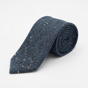Puede incluir: Una corbata azul oscuro con un patr&oacute;n texturizado y moteado con peque&ntilde;as motas blancas y negras por toda la tela. La corbata est&aacute; enrollada en forma de espiral, mostrando claramente el material tejido y el extremo puntiagudo de la corbata.