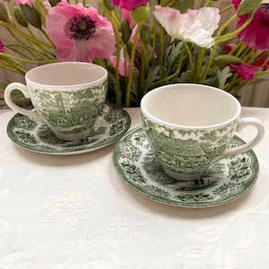 Może przedstawiać: Zestaw trzech ceramicznych kubków z nakrapianym, matowym wykończeniem. Kubki są w odcieniach kremu, jasnoszarym i ciemnoszarym. Każdy kubek ma prosty, minimalistyczny design.