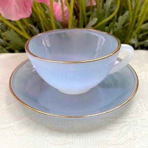 Puede incluir: Una taza de cerámica blanca con un asa negra y el texto "But First, Coffee" en negrita negra. La taza está sobre un fondo borroso. La taza mide aproximadamente 10 cm de altura.