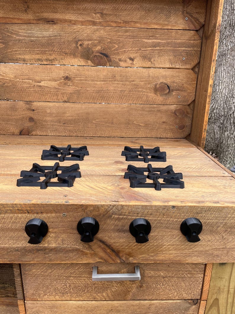 May include: A rustic wooden outdoor kitchen with four black cast iron burner grates and three black knobs. The kitchen has a drawer with a silver handle.
