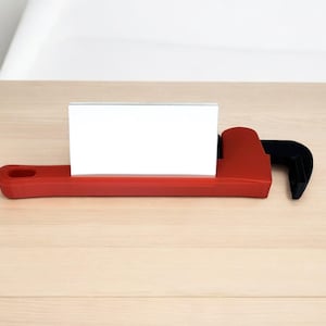 May include: A red and black wrench-shaped business card holder. The holder has a slot for a business card and is made of plastic.