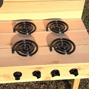 May include: A wooden play kitchen with four black electric stove burners. The play kitchen is made of light-colored wood and has black knobs. The kitchen is designed for children to play with.