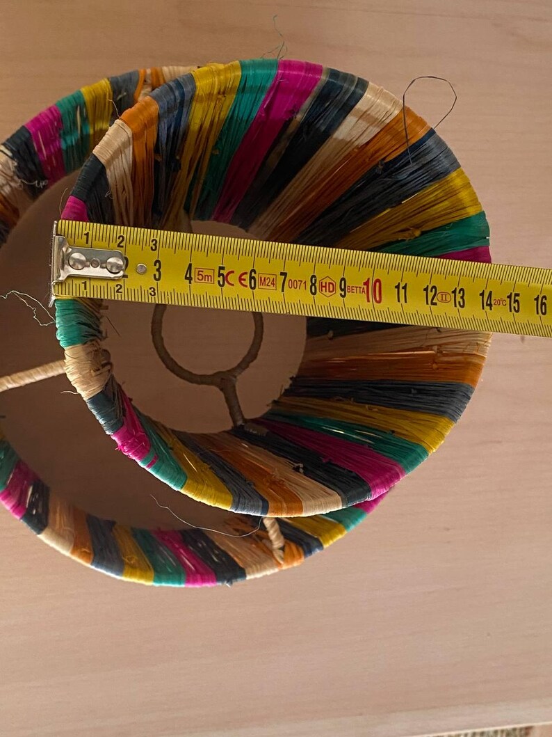 May include: A double-layered lampshade made of woven colorful strips of fabric. The lampshade is approximately 10 inches in diameter.