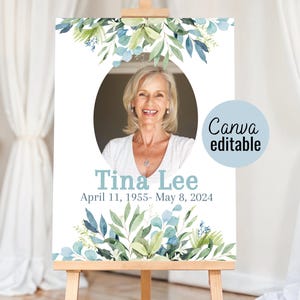 May include: A white memorial sign with a photo of a woman in a light blue oval frame. The sign has a green and blue floral design at the top and bottom. The text on the sign reads "Tina Lee, April 11, 1955 - May 8, 2024".