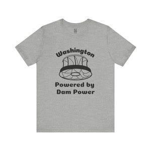 May include: A heather gray t-shirt with the text "Washington" above a graphic of a dam and the words "Powered by Dam Power" in black. The shirt is a short-sleeved crew neck.