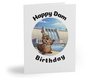 May include: A white greeting card with the words "Happy Dam Birthday" in black. The card features a cartoon beaver wearing a party hat and bow tie, standing in front of a dam illustration.