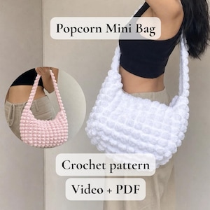 Può includere: Due borse Popcorn Mini, una bianca e una rosa, realizzate all'uncinetto con un punto strutturato. Le borse hanno una forma arrotondata e una tracolla. L'immagine include anche il testo "Crochet pattern" e "Video + PDF".