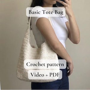 Op de afbeelding: Crèmekleurige gehaakte tote bag met een schouderband. De tas heeft een gestructureerd steekpatroon en is gelabeld met "Basic Tote Bag", "Crochet pattern" en "Video + PDF". De tas wordt door een persoon gedragen.