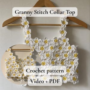 Pode incluir: Um top de crochê branco com detalhes de margaridas amarelas, exibido em um cabide de madeira. O top apresenta um design de gola Granny Stitch. O texto na imagem diz "Granny Stitch Collar Top" e "Crochet pattern Video + PDF".