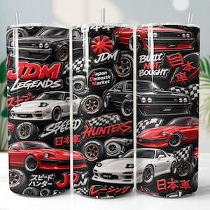 May include: A black tumbler featuring a collage of Japanese sports cars in red, white, and black. The design includes text such as "JDM Legends", "Built Not Bought", and Japanese characters. The tumbler has a silver straw.