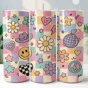 Puede incluir: Un vaso cilíndrico con pajita que presenta un patrón de cuadros en tonos pastel rosa, azul, amarillo y morado. El diseño incluye varios iconos como margaritas, caras sonrientes, un sombrero de vaquero, una bola de discoteca, corazones y paz.