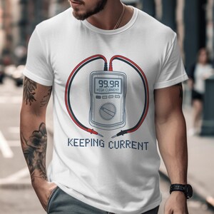 May include: White t-shirt with a graphic of a digital multimeter displaying "99.9A HIGH CURRENT". The design includes red and black wires forming a circle around the meter, with the text "KEEPING CURRENT" below.