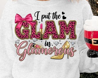 May include: A light gray sweatshirt with a graphic design that reads "I put the GLAM in Glamorous." The word "GLAM" is in pink leopard print with a gold outline. The design includes a pink bow, lipstick, diamonds, and a gold glitter high heel.